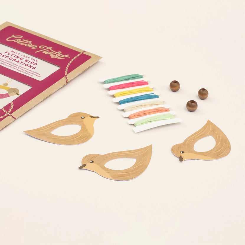 Wooden bird-shaped decorations with colorful strings and packaging on a light background