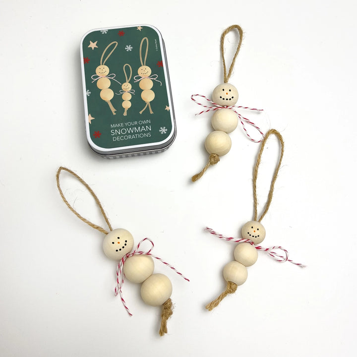 Wooden snowman decorations with a tin labeled 'Make Your Own Snowman Decorations' on a white background.