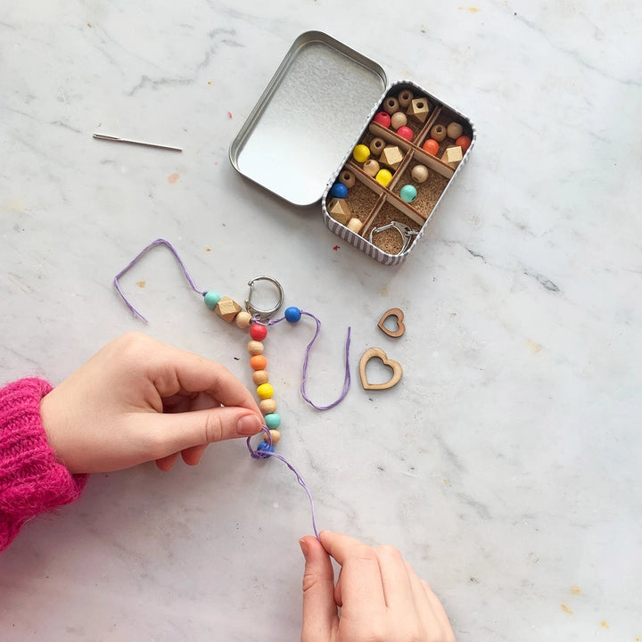 Childs hands making a beaded keyring with a small metal bead box on a marble surface