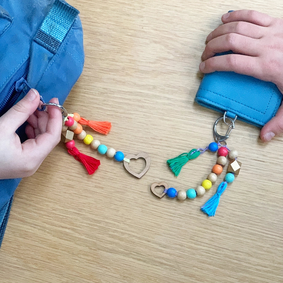 Colourful keychain from Cotton Twist craft kit with beads and tassels attached to a blue bag on a wooden surface.