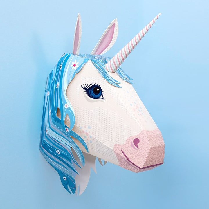 A paper craft unicorn head mask with a white textured face, pink nose and horn, blue hair, and a light blue background.