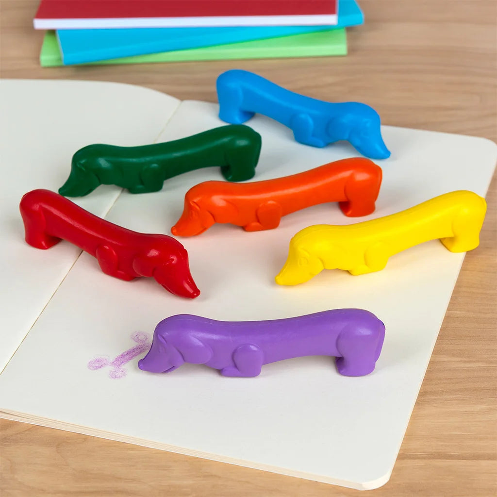 Colourful dog-shaped crayons on a wooden surface with books in the background