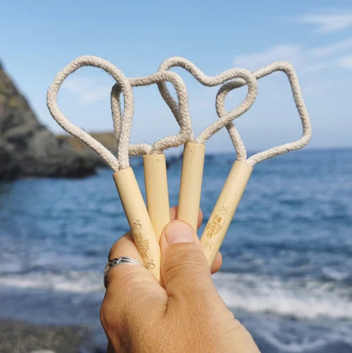 hand holding up 4 dr zigs mini bubble wands with cotton loop and wooden handle. The sea and coastline is in the background. 