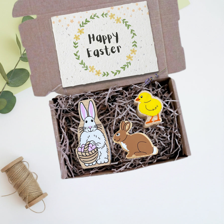 Easter-themed wooden play figures in a box with a 'Happy Easter' card on a light background