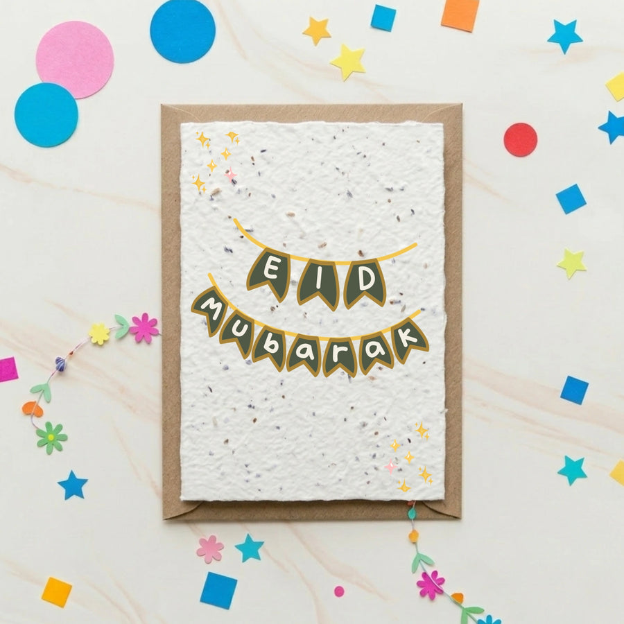 Greeting card with 'Eid Mubarak' text on a textured white paper, surrounded by colourful confetti on a light wooden surface.