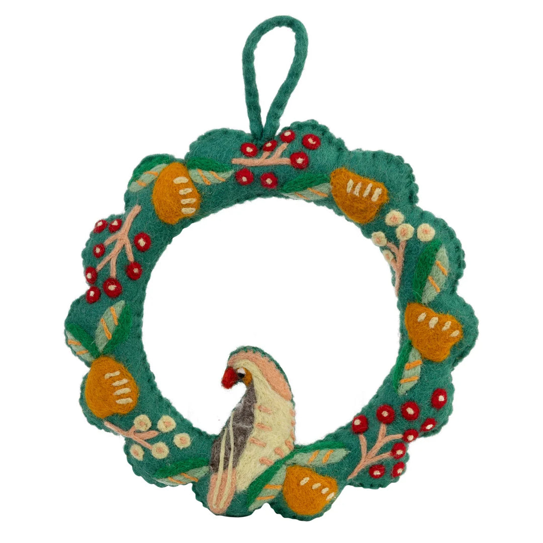 A green felt Christmas wreath ornament with embroidered orange pumpkins, red berries, white berries, and a felt bird at the bottom, hanging by a green loop on a white background.