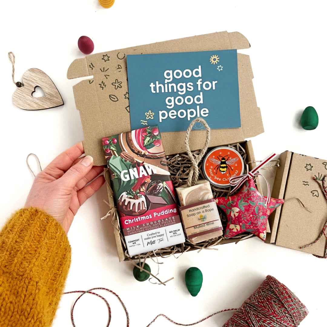 Gift box with festive items including christmas pudding chocolate bar, mulled wine soap, seedballs and a decoration. The box has a card reading 'good things for good people' on a white background.
