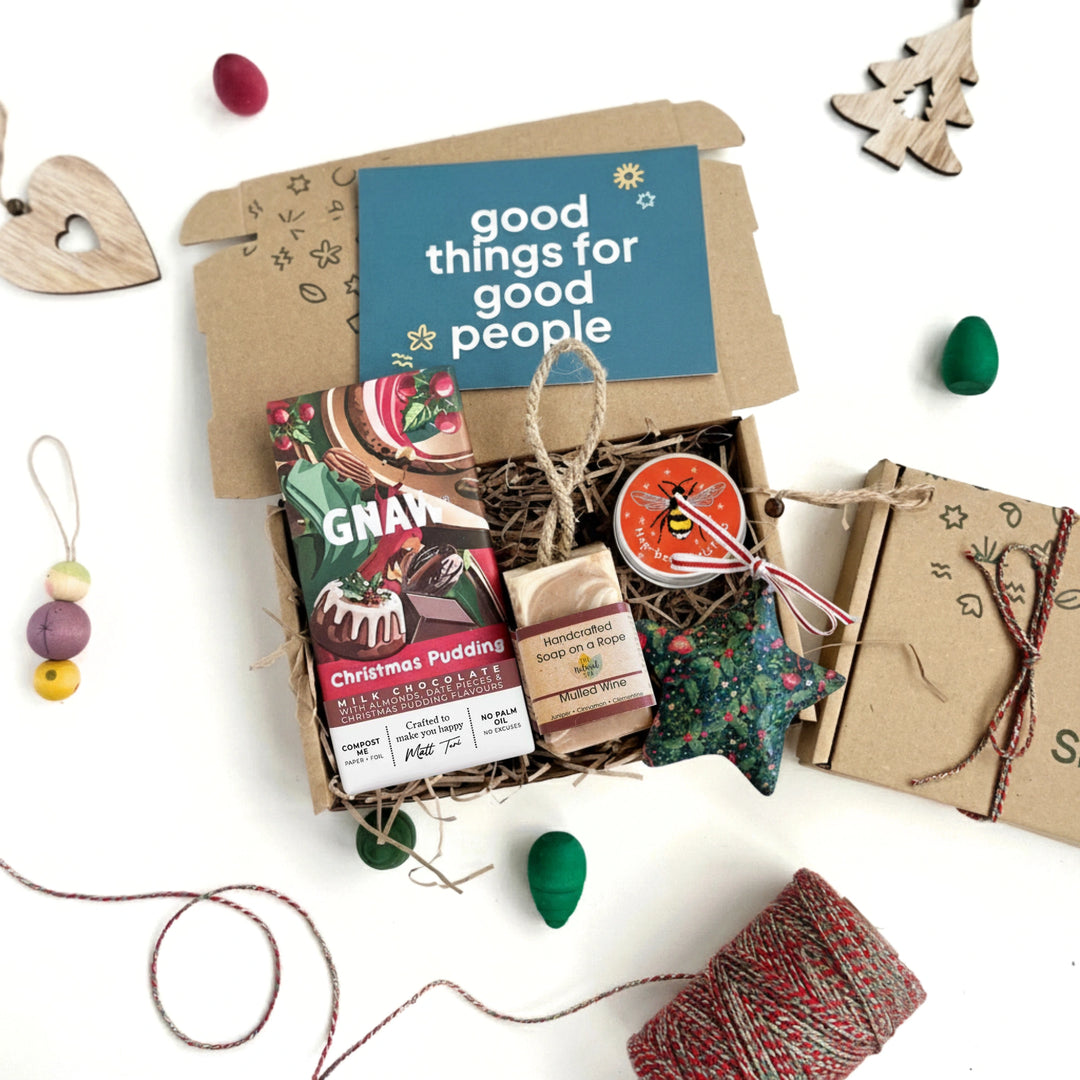 Gift box with Christmas-themed items and a card reading 'good things for good people' on a white background.