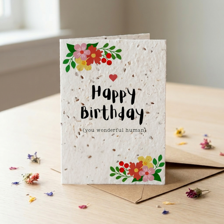 happy birthday plantable seed card with colourful floral design standing on a wooden table with a kraft paper envelope