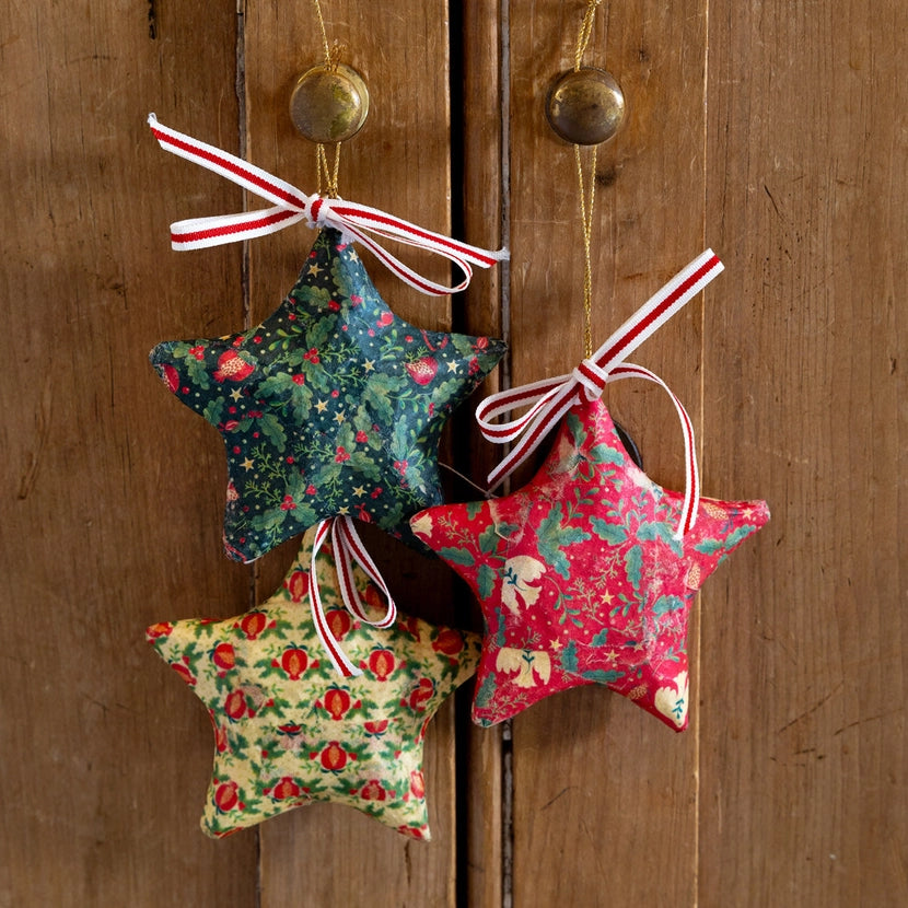 Three star-shaped fabric ornaments with floral patterns hanging on a wooden door.