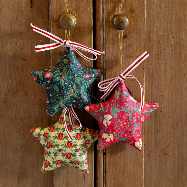 Three star-shaped fabric ornaments with floral patterns hanging on a wooden door.