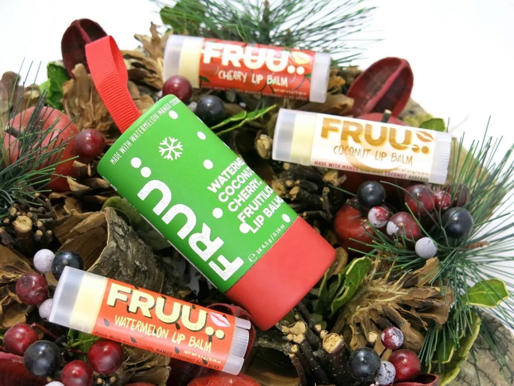 three fruity lip balms and a red and green Christmas gift tube on some festive foliage with berries. 