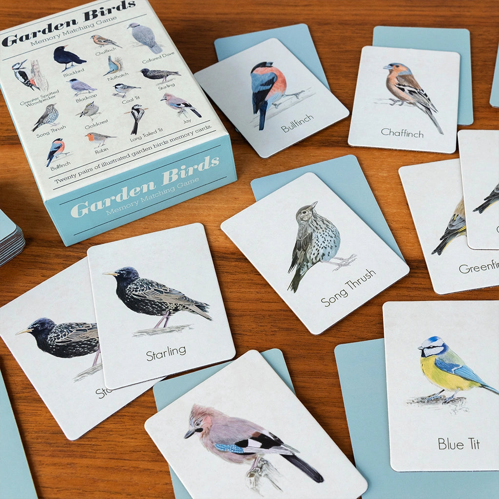 Illustrated cards from the rex London garden birds memory game laid out on a wooden table with a printed gift box