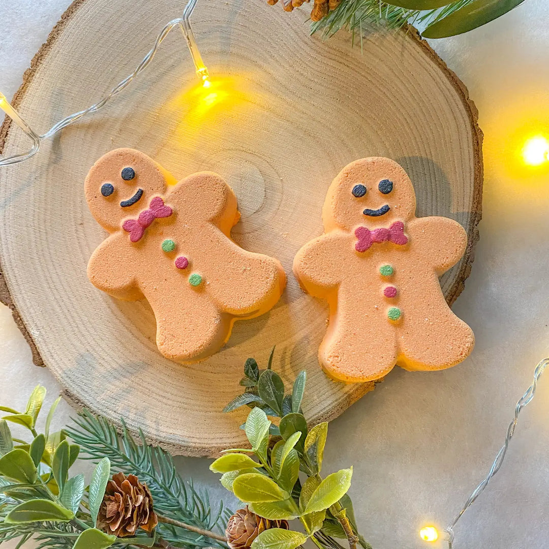 two gingerbread man bath bombs on a log slice with Christmas lights 