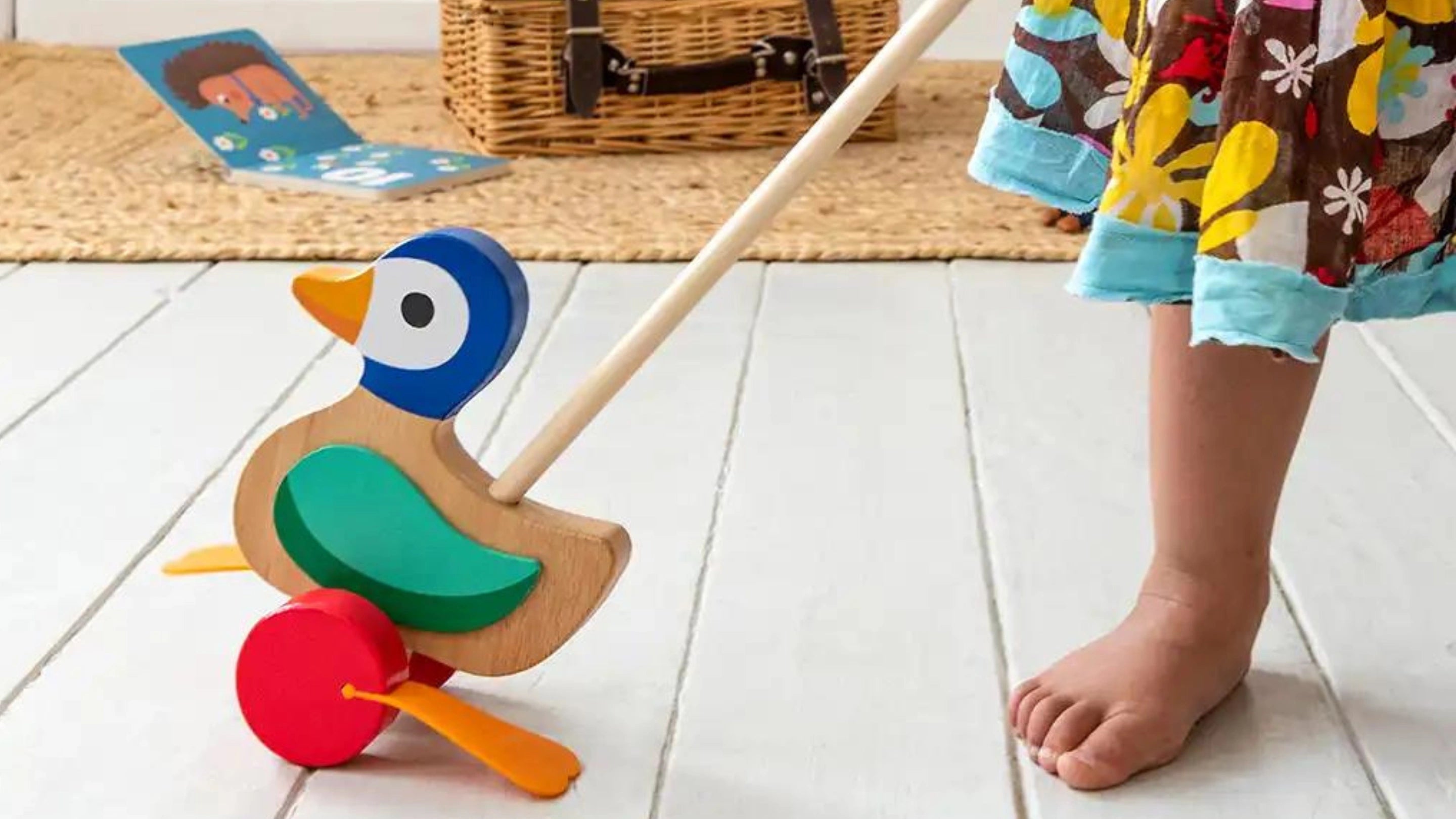 little girl with bare feet wearing a floral skirt and pushing a colourful wooden push along duck