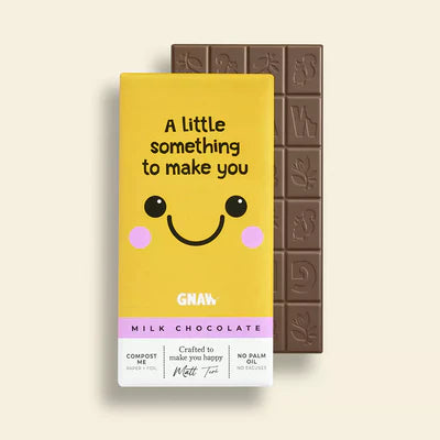 'Something to Make You Smile' Milk Chocolate Bar in a yellow wrapper with a cute smiley face. A bar of milk chocolate is in the background. 