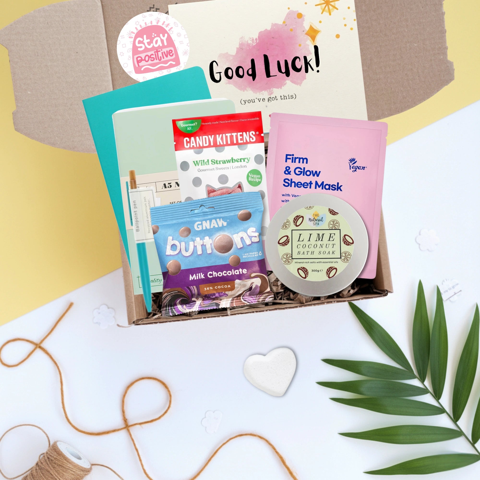 Assorted products including a sheet mask, candy, and chocolate in a box with good luck card on a decorative background.