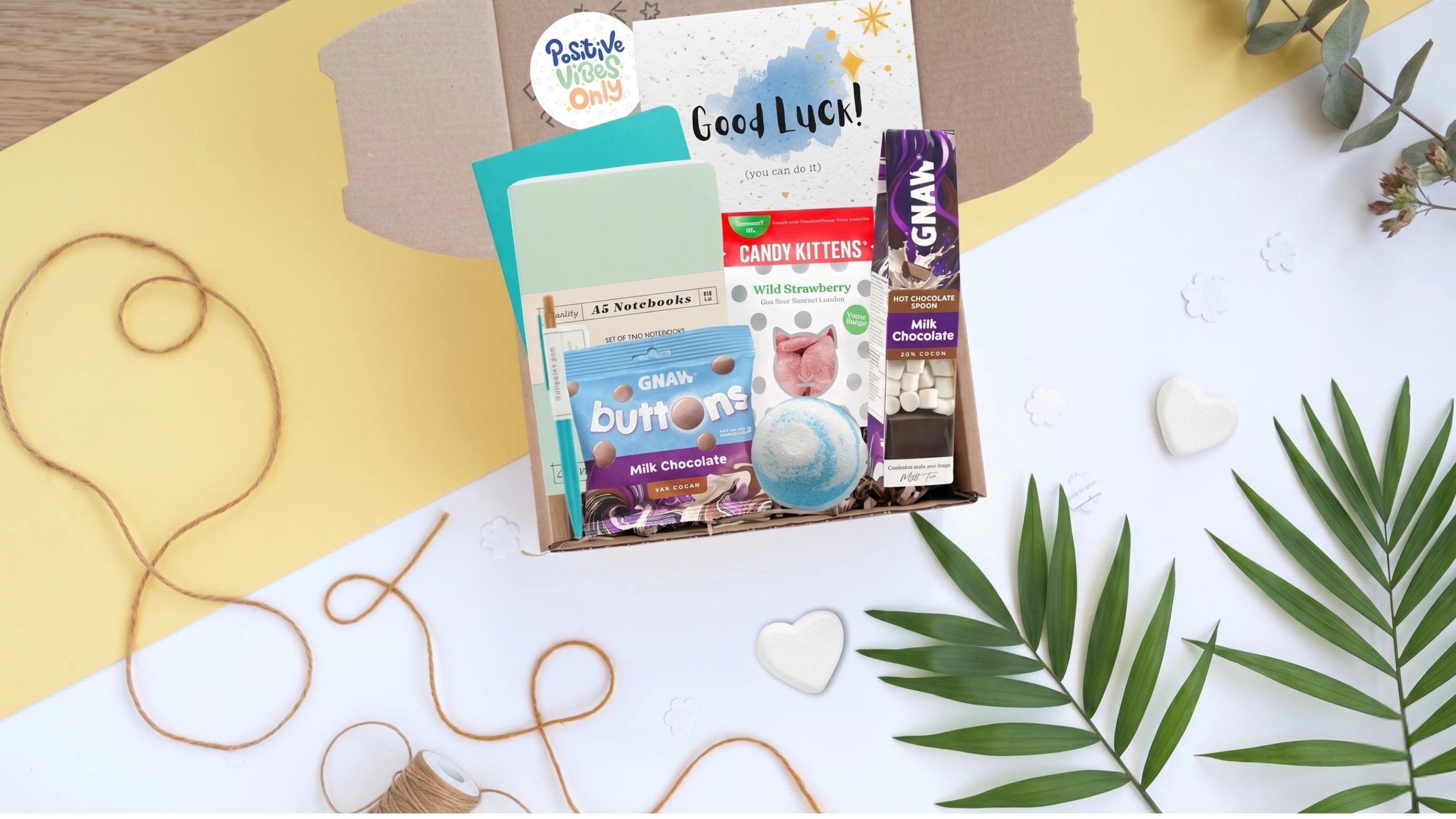 Assorted products including a box of chocolates, a magazine, and a tube of toothpaste on a decorative surface with leaves and heart shapes.