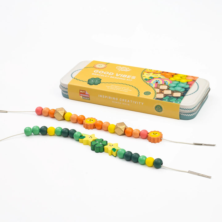 A wooden bead craft kit with colorful wooden beads on strings, shown in front of its yellow metal storage tin on a clean white background. The tin is labeled &