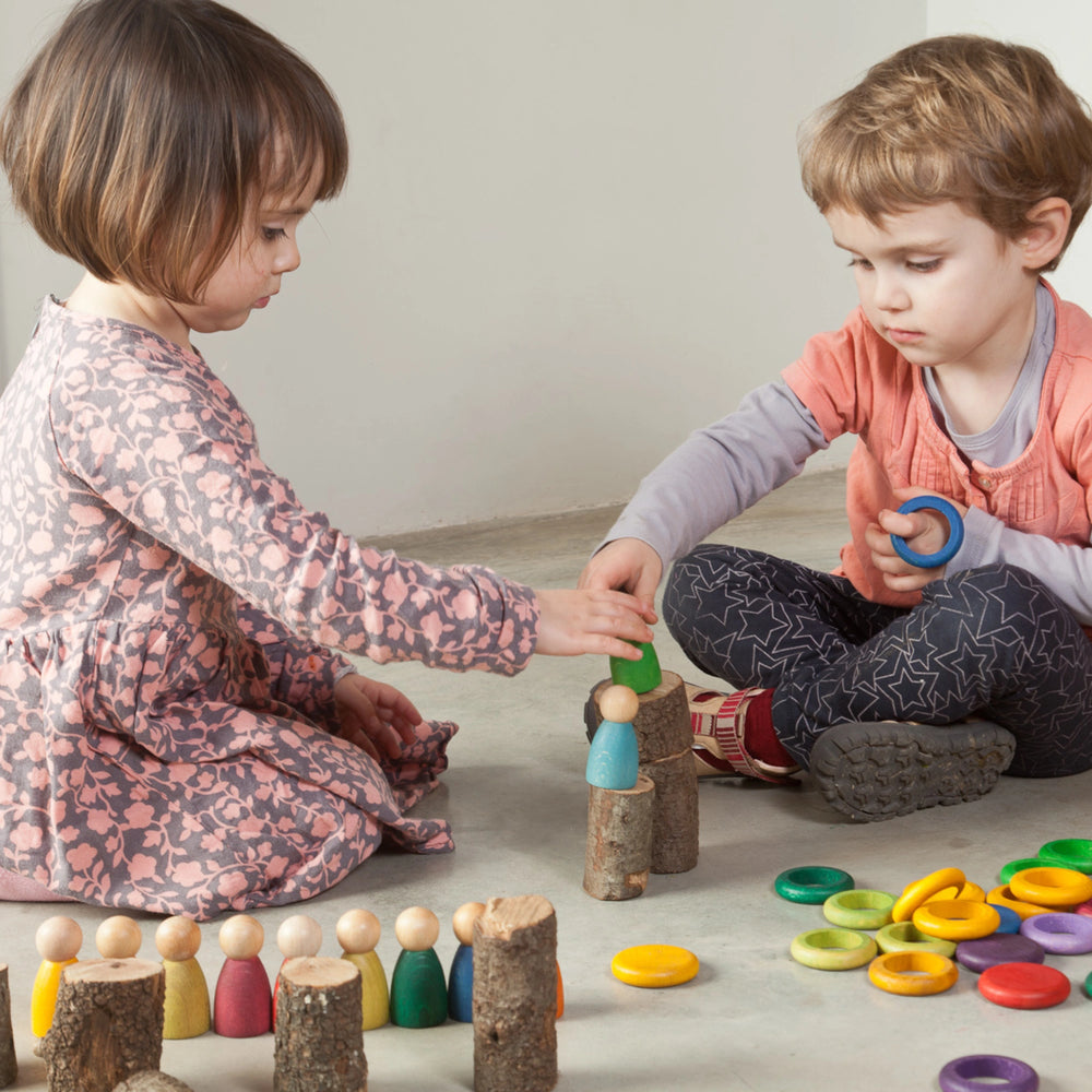 Two children playing with a Grapat 12 nins play set and other wooden toys on a coloured floor.