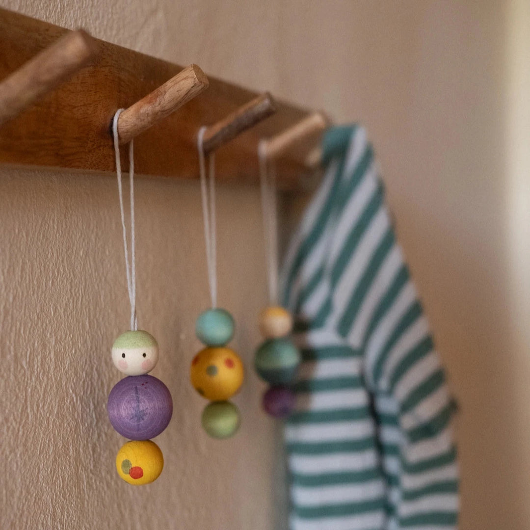 set of 3 Snowy Buddy wooden Christmas decorations hanging on wooden hooks. The decorations, by Grapat toys are painted to look like people with colourful patterns and little eyes