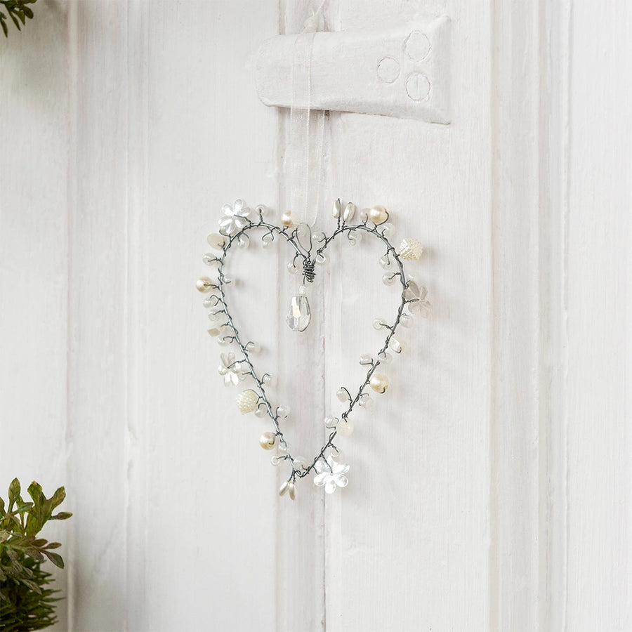 beaded heart decoration in white and silver hanging from a white door