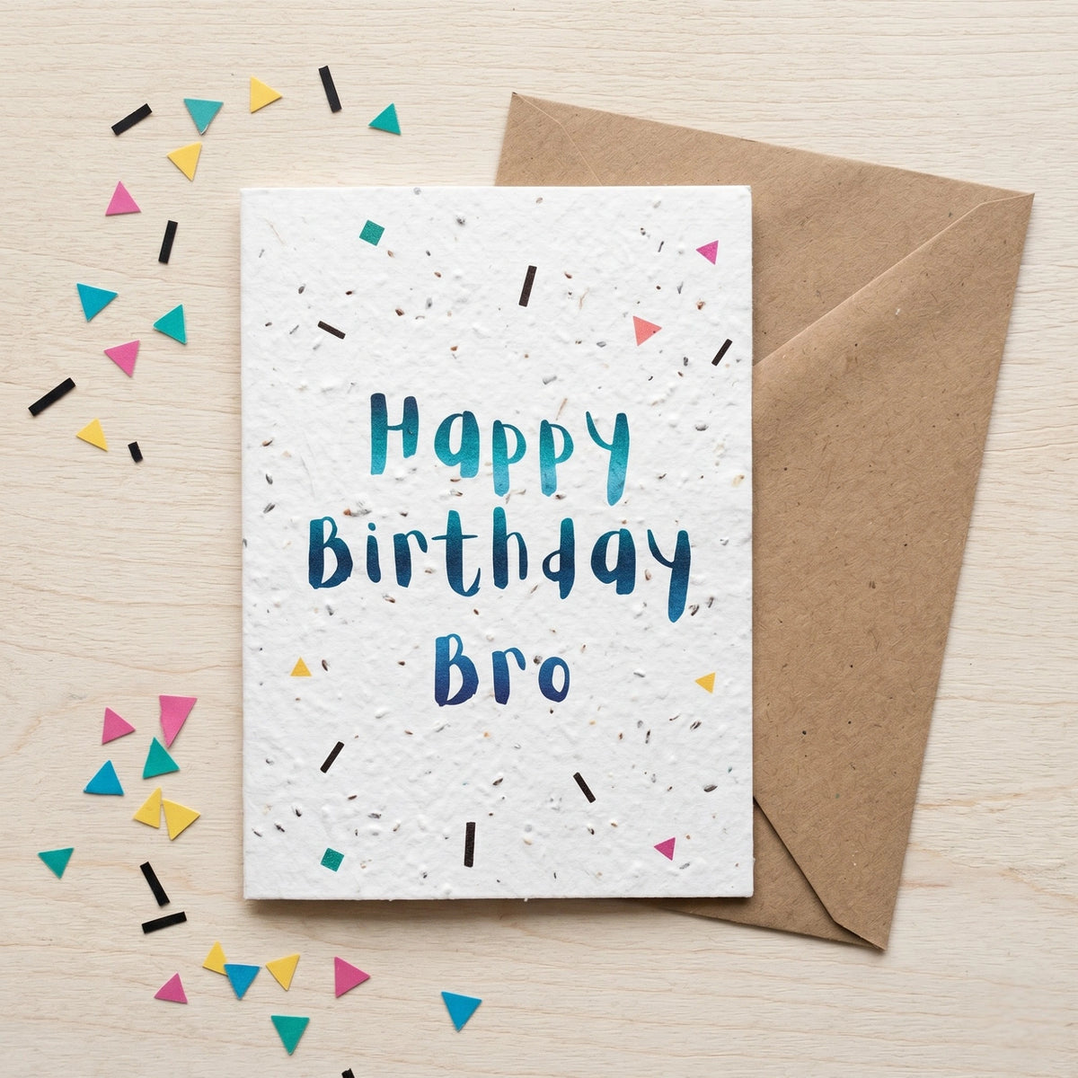 Birthday card for 'Bro' with colourful confetti and a brown envelope on a light wood background