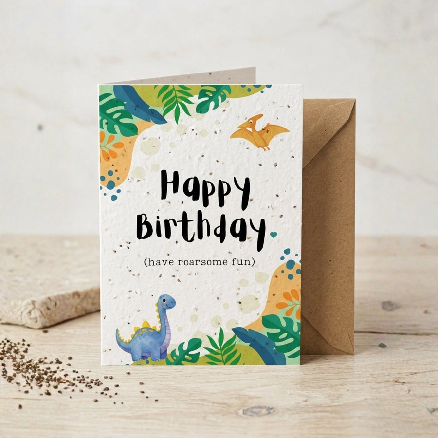 Birthday card with dinosaur illustrations and 'Happy Birthday (have roarsome fun)' text on a wooden surface.