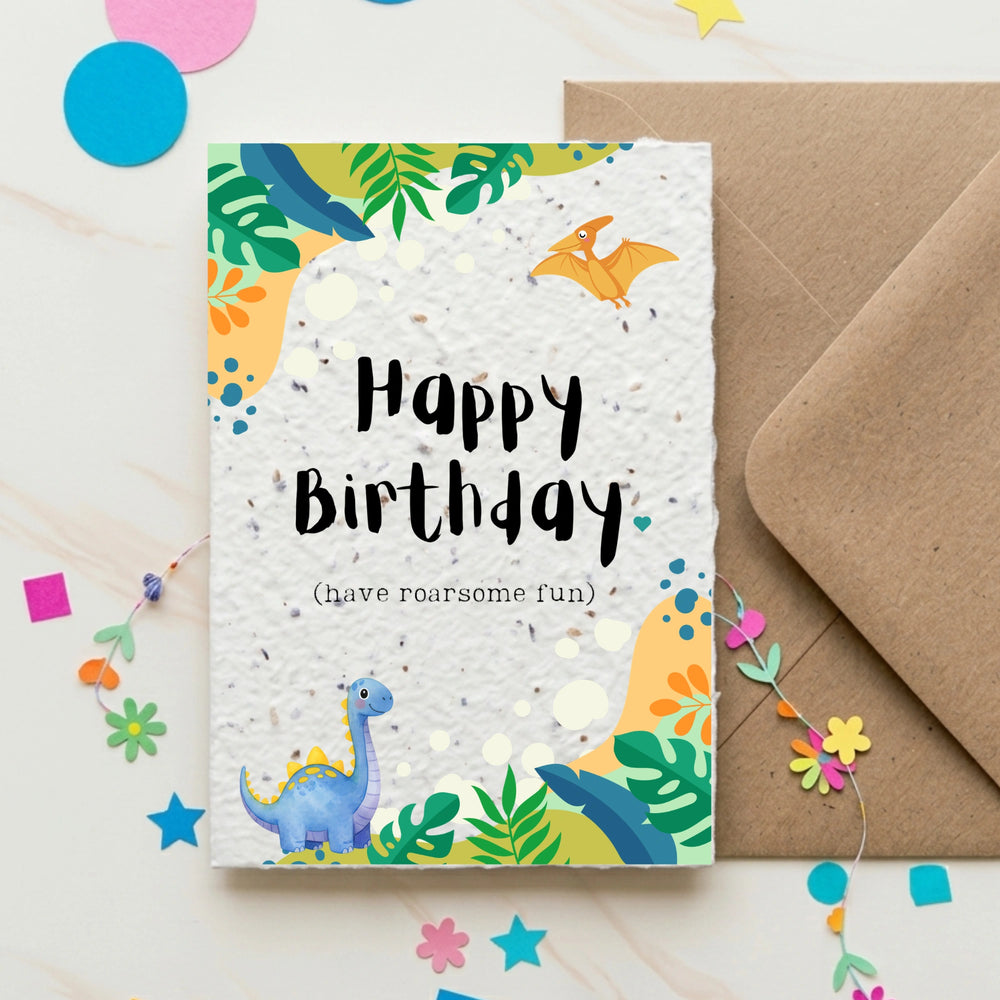 Birthday card with dinosaur illustration and 'Happy Birthday' text, accompanied by a brown envelope on a colourful background.