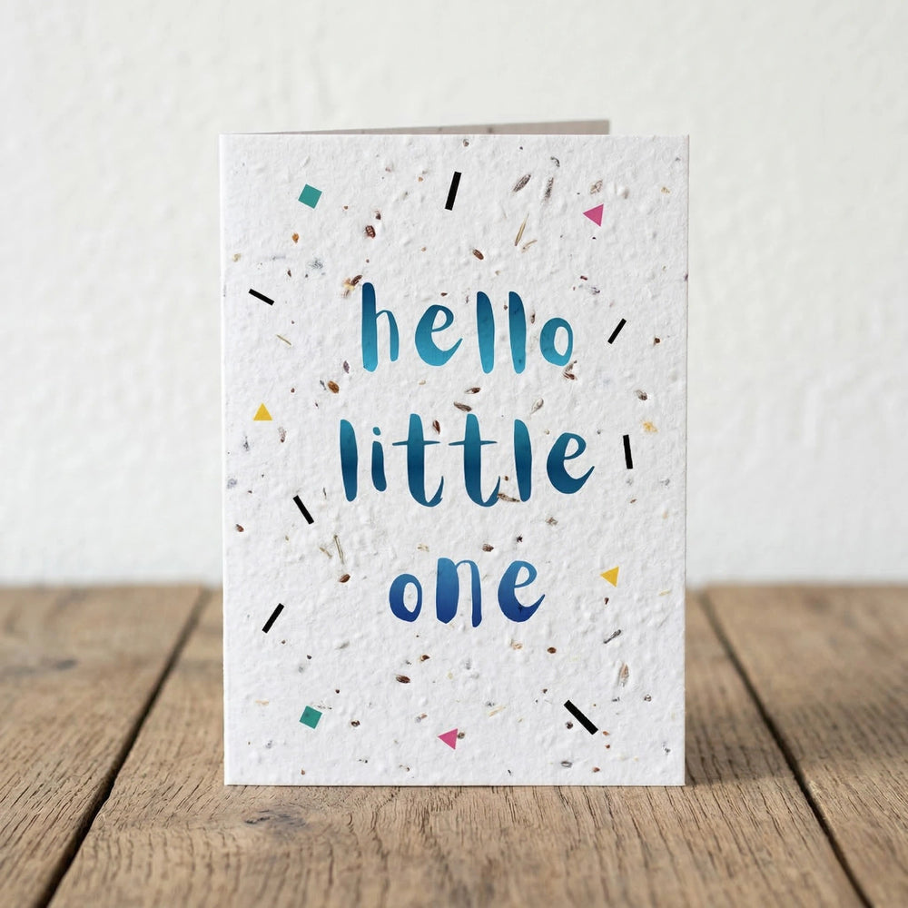 Greeting card with 'hello little one' text on a textured white background, placed on a wooden surface.