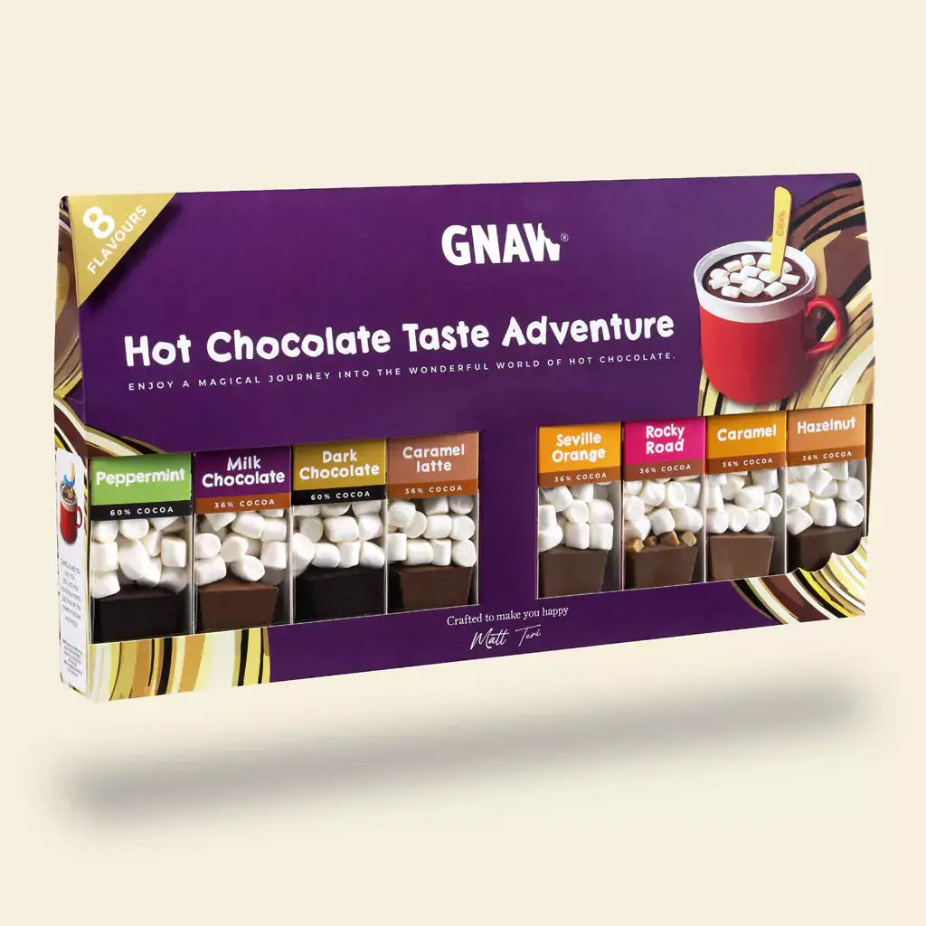A boxed hot chocolate flavour adventure set by GNAW, featuring a purple package with multiple small chocolate cups labeled with different flavours including peppermint, milk chocolate, dark chocolate, caramel latte, sev-lite, orange, caramel, and hazelnut. The box is shown floating against a light beige background.
