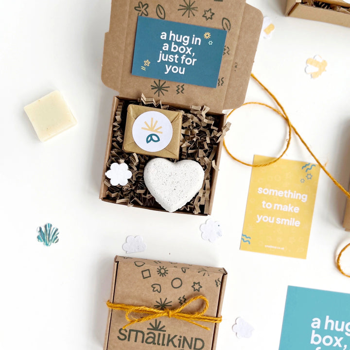 Small gift box with heart-shaped bath bomb, mini soap bar and 'a hug in a box, just for you' card on a white background.