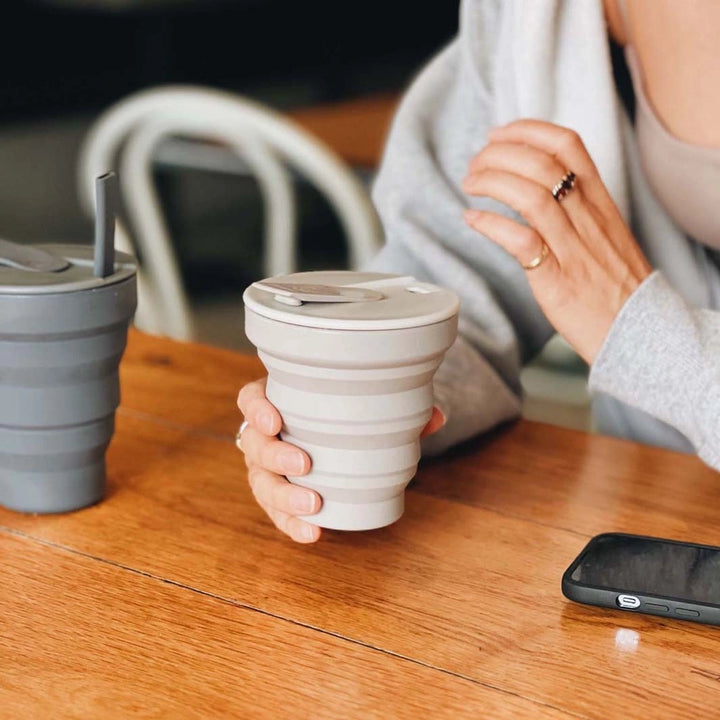 womans hand holding a Hunu warm grey collapsible travel coffee cup