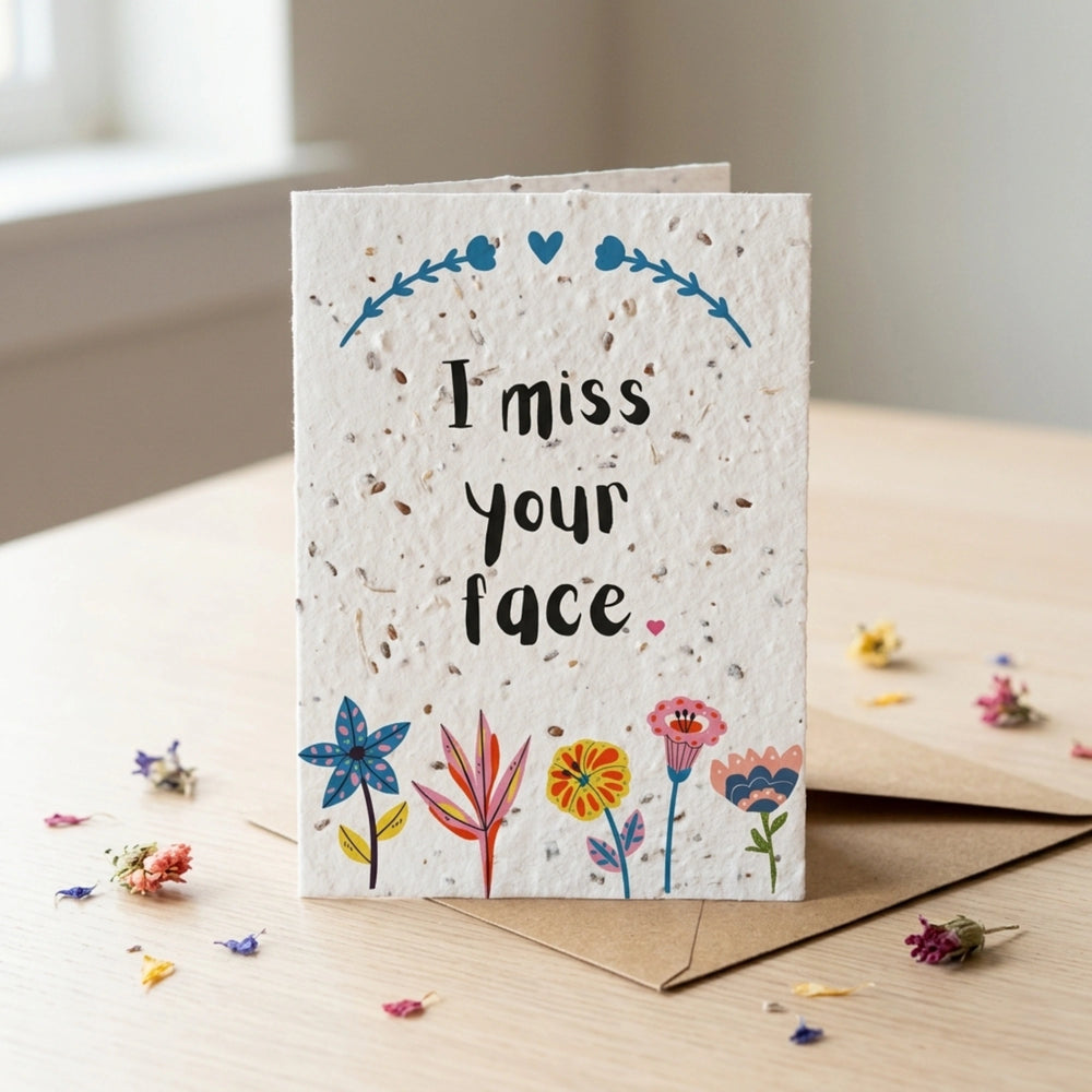 Greeting card with 'I miss your face' text and floral designs on a wooden surface.