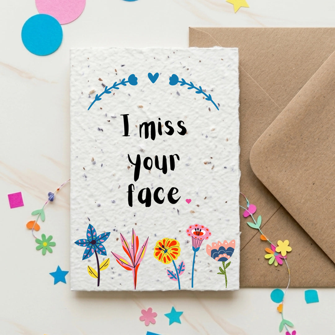 Greeting card with 'I miss your face' text and colorful flowers, accompanied by a brown envelope on a decorative background.