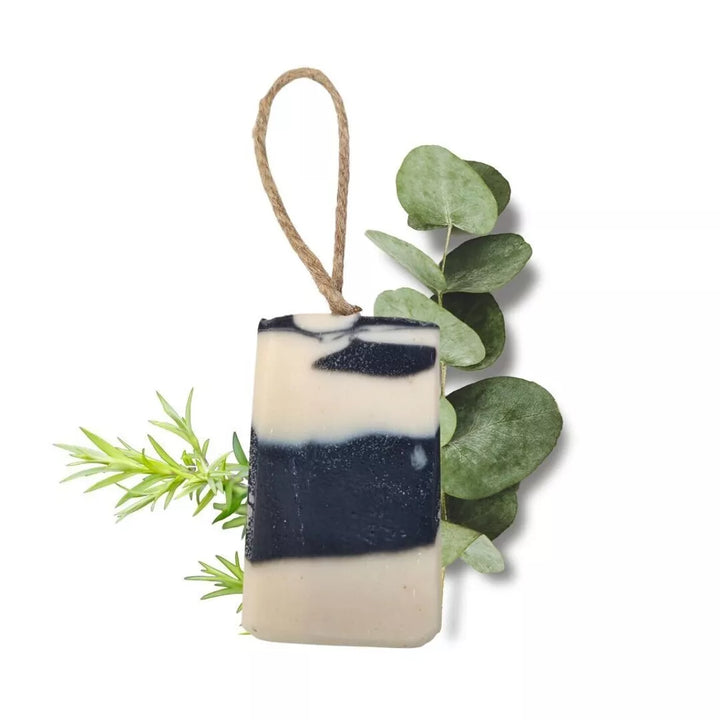 Bar of soap with a rope, surrounded by green leaves on a white background