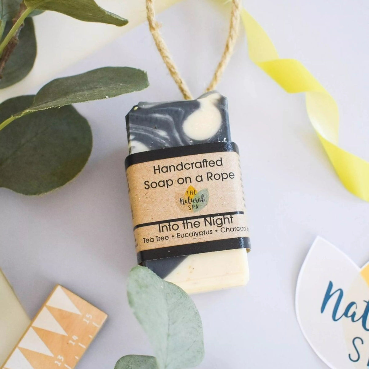Handcrafted soap on a rope with green leaves and decorative elements on a light background