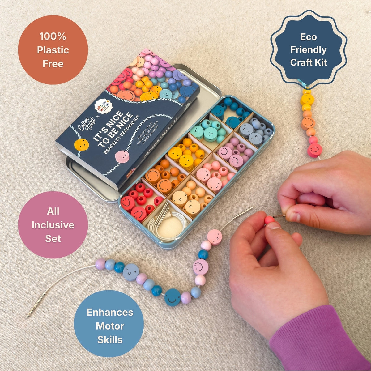 A children's craft kit shown on a light beige surface with a person's hands actively making a beaded bracelet. The kit includes a tin of colorful wooden buttons, a box of craft supplies, and finished example bracelets.
