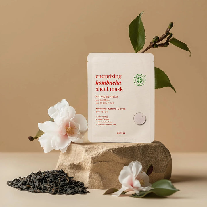 Energizing kombucha sheet mask on a stone block with flowers and tea leaves on a beige background