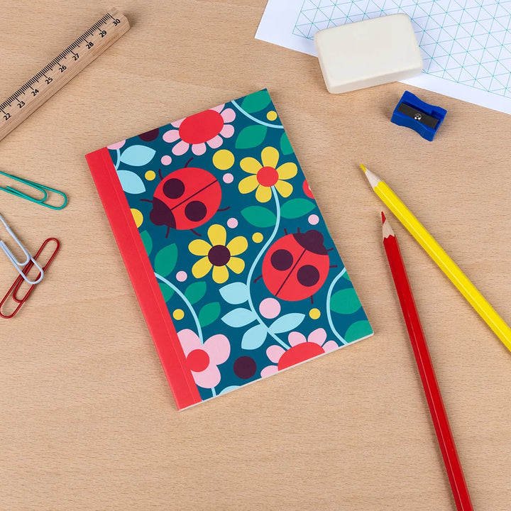 small notebook with ladybird and flower design on a desk with colourful pencils and stationery items