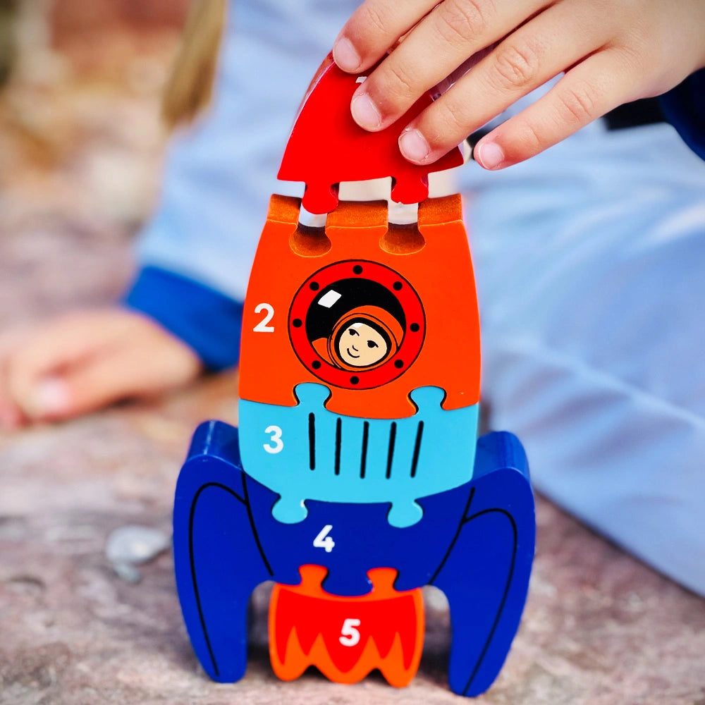 child playing with the Lanka Kade wooden rocket puzzle with five brightly coloured pieces in red, orange, blue and purple. The pieces are numbered 1 to 5 to help with counting. For children 10 months and over.