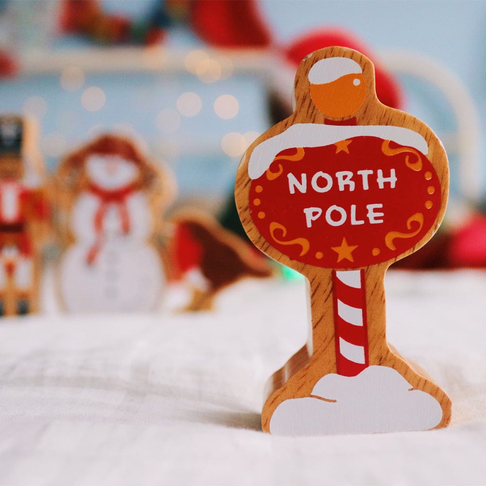 wooden North Pole sign play figure with other wooden Christmas figures in the background 