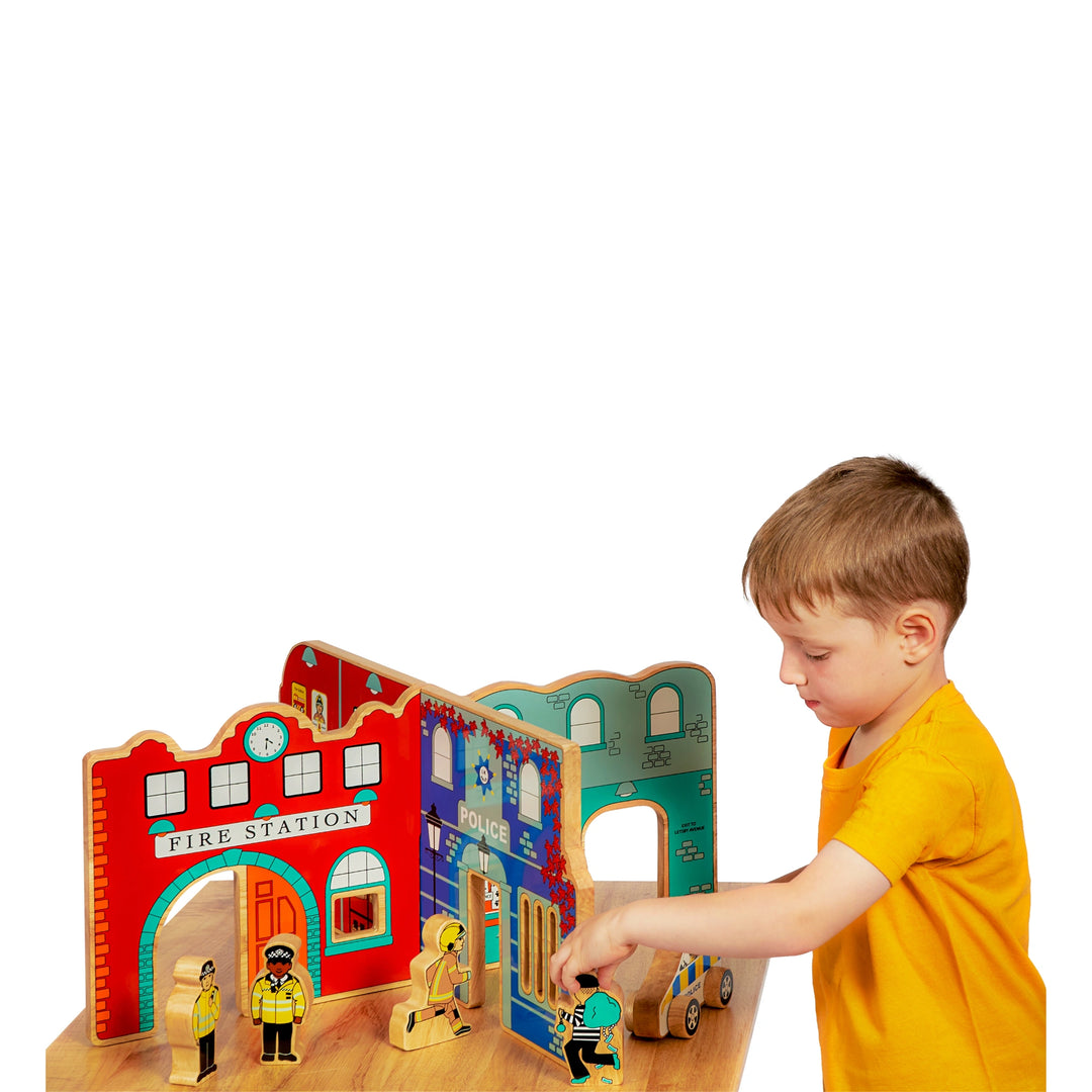 Child playing with a wooden toy fire and police station set on a white background