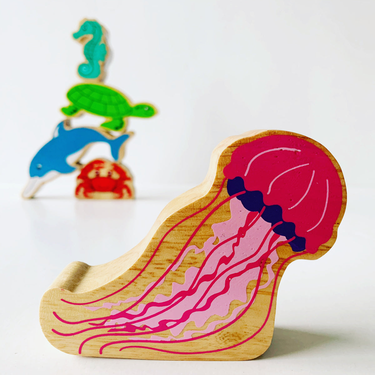 Lanka Kade Wooden Jellyfish with painted details and a wood grain edge. There are crab, dolphin, turtle and seahorse play figures in the background. 
