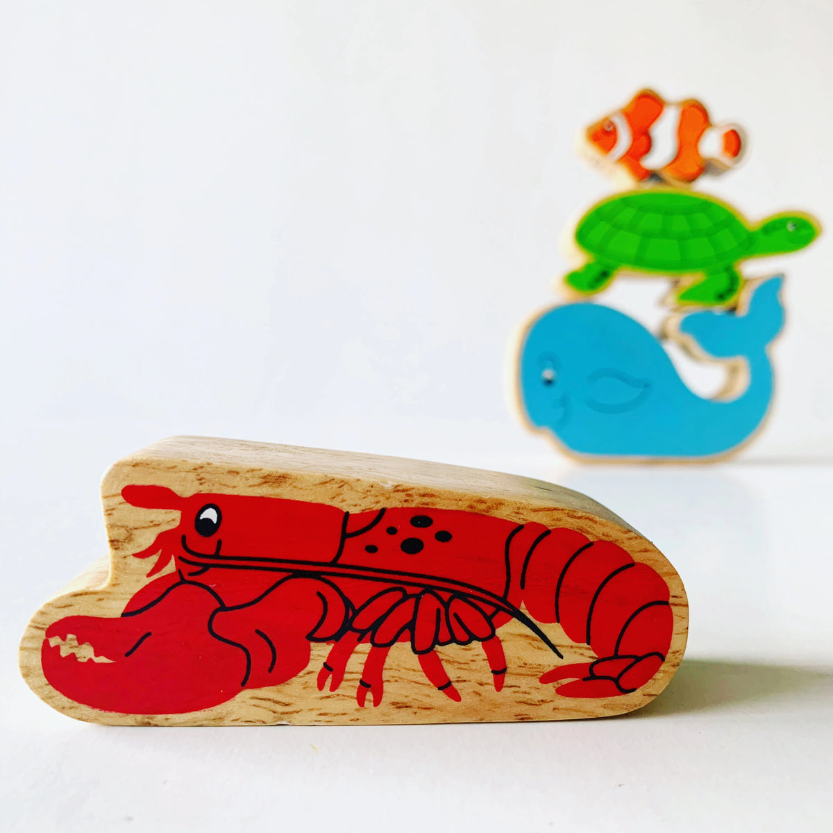  Lanka Kade Wooden Lobster play figure with painted details and a natural wood grain edge. Turtle, whale and clownfish play figures are in the background. 