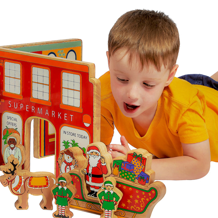 Child playing with a wooden toy supermarket set on a white background with christmas characters in the foreground