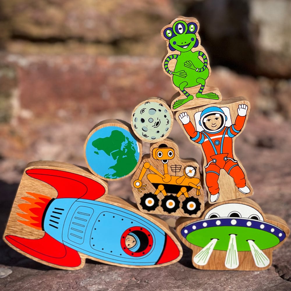 set of 7 space themed wooden play figures stacked up with rocks in the background. age 10 months+
