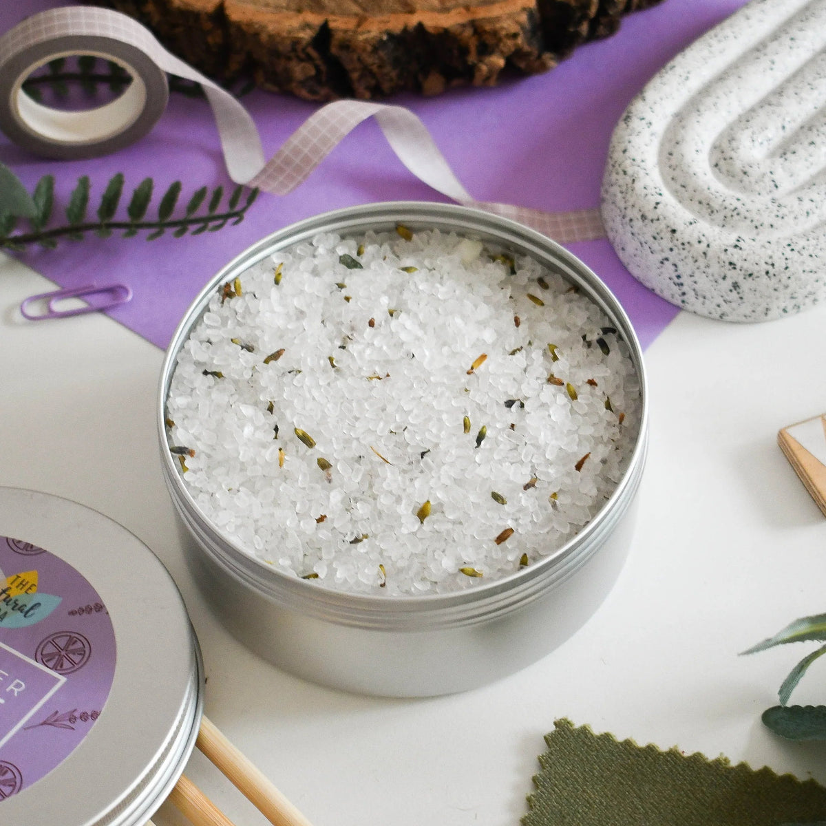 Metal tin filled with bath salts on a wooden surface with decorative items.
