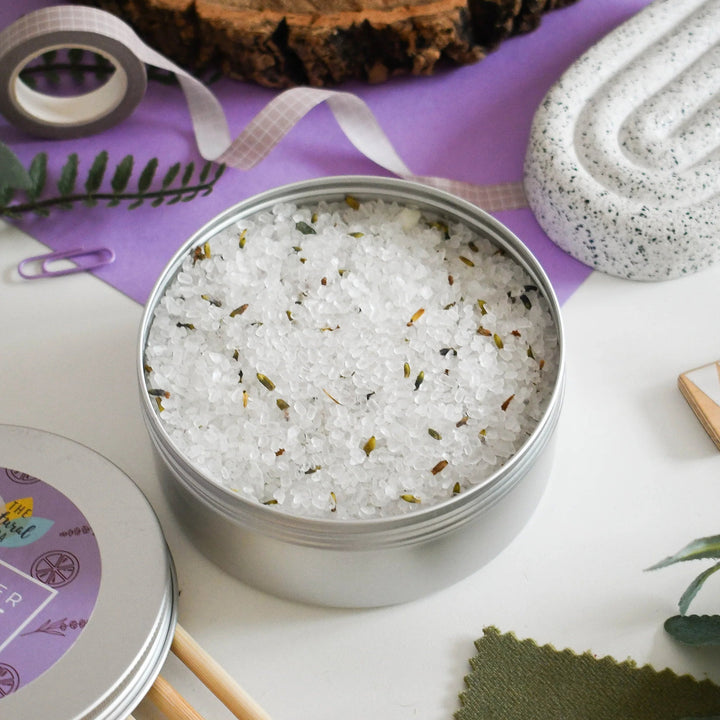 Metal tin filled with bath salts on a wooden surface with decorative items.