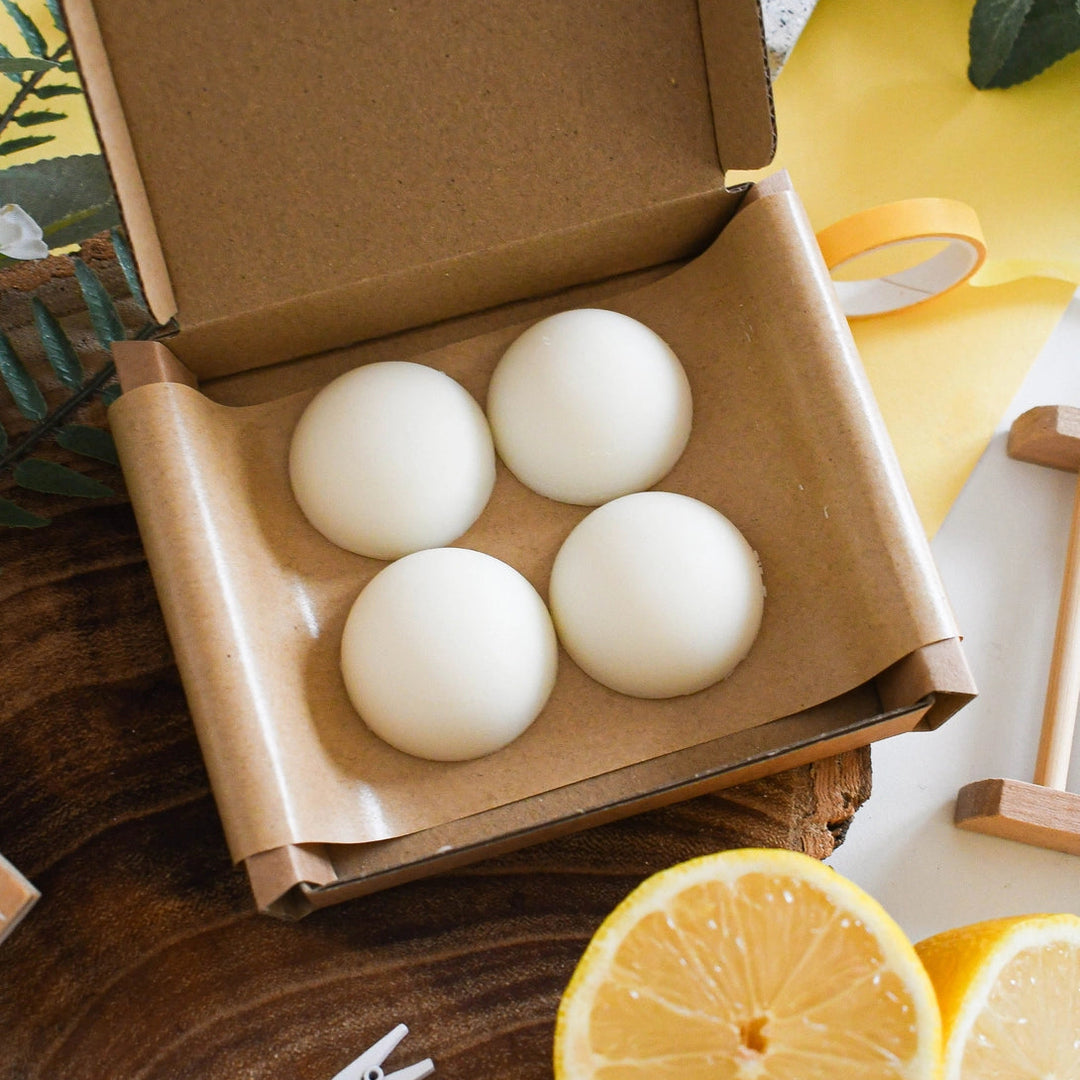 four round wax melts in a kraft gift box laid on a lemon yellow surface with lemon slices 